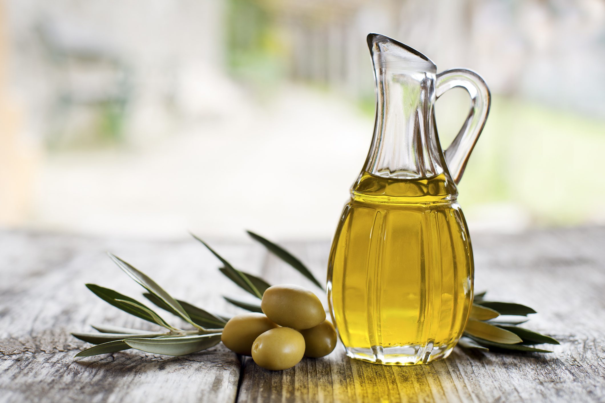 A glass pitcher of olive oil sitting on top of a wooden table.